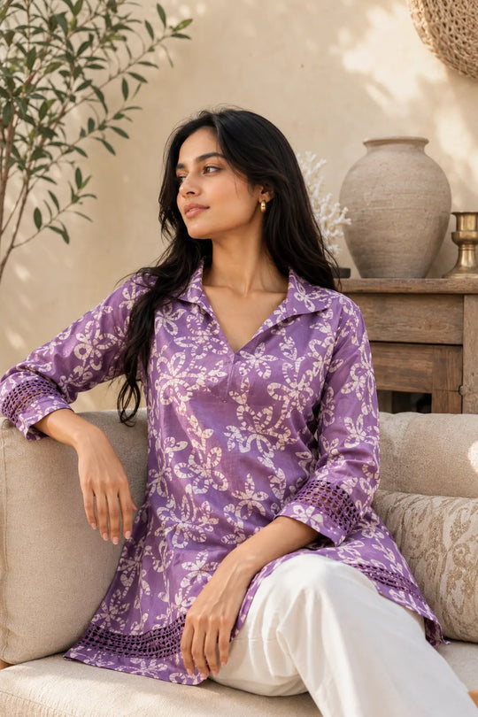 A soft lavender cotton tunic shirt featuring an intricate all-over floral Batik print, classic shirt collar, relaxed silhouette, and 3/4th sleeves with delicate lace detailing. Finished with lace accents at the hem for a subtle handcrafted touch. Lightweight, breathable, and easy to style, it is perfect for workdays, casual outings, and effortless everyday dressing.